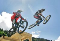 Zwei Mountainbiker springen über eine Schanze