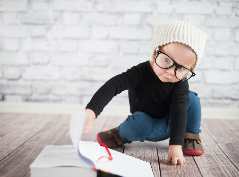 Junge mit cooler Brille und Haube blättert vor einer Ziegelmauer in einem Buch