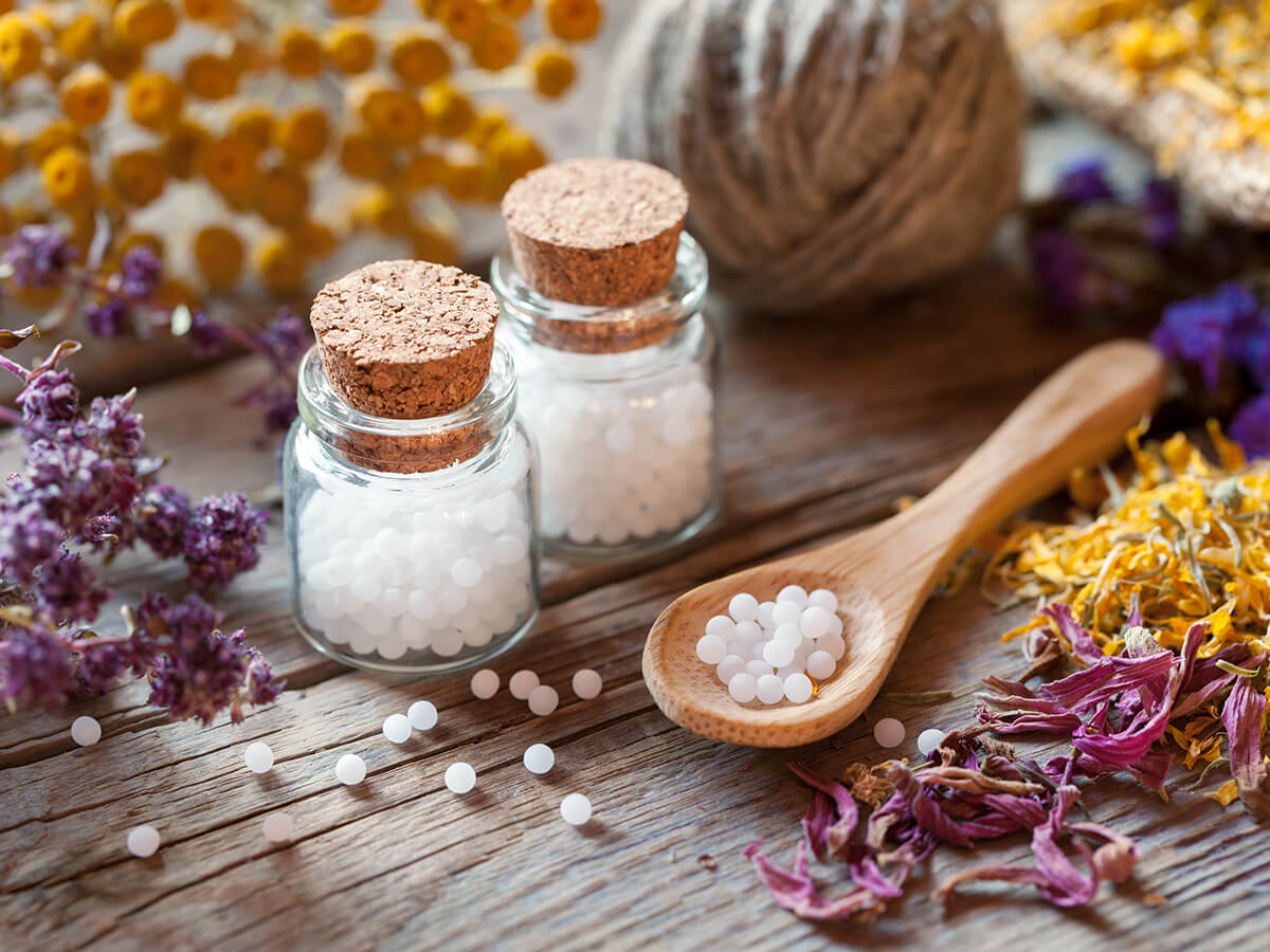 Homöopathische Zutaten (Pflanzen) und Globuli auf einem Holzlöffel