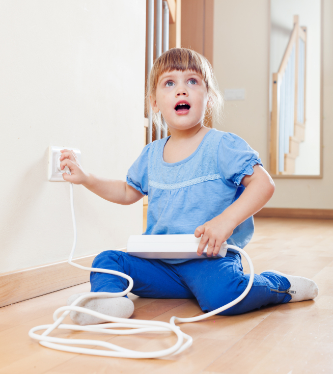Mädchen spielt mit Steckdosenleiste und Steckdose an der Wand