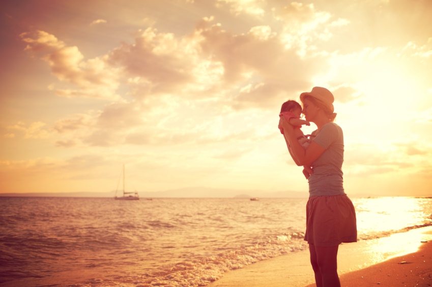 Mutter mit Tochter im Arm im Sonnenuntergang auf einem Strand