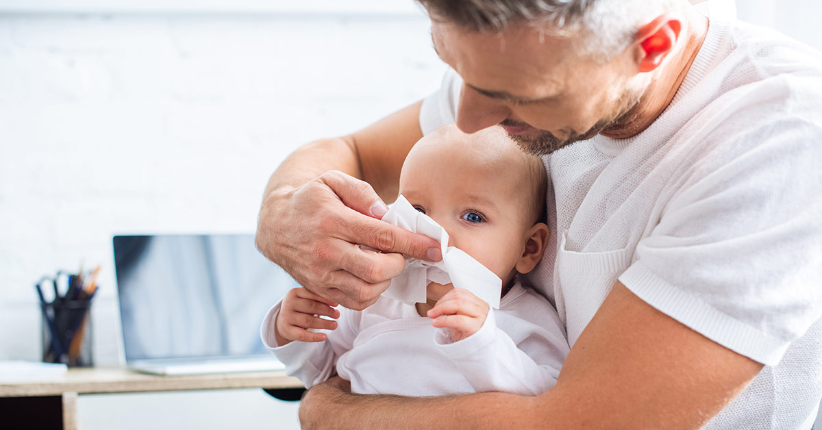 Vater hilft einem Baby beim Schneuzen