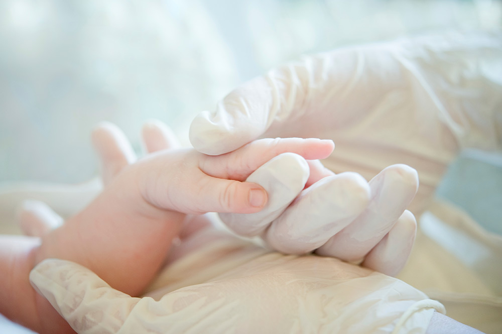 Arzthand mit Handschuh hält eine Kinderhand