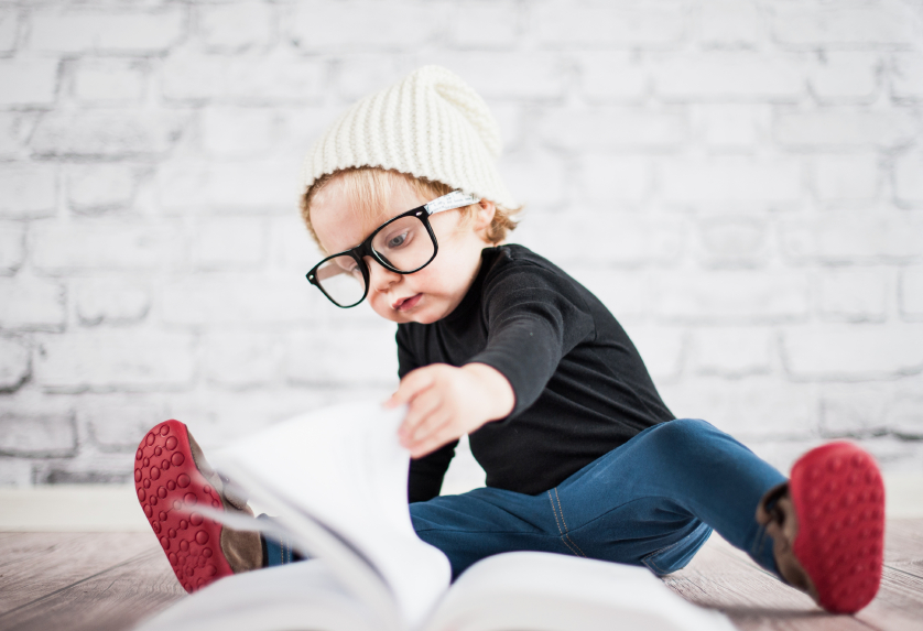 Junge mit cooler Brille und Haube blättert vor einer Ziegelmauer in einem Buch